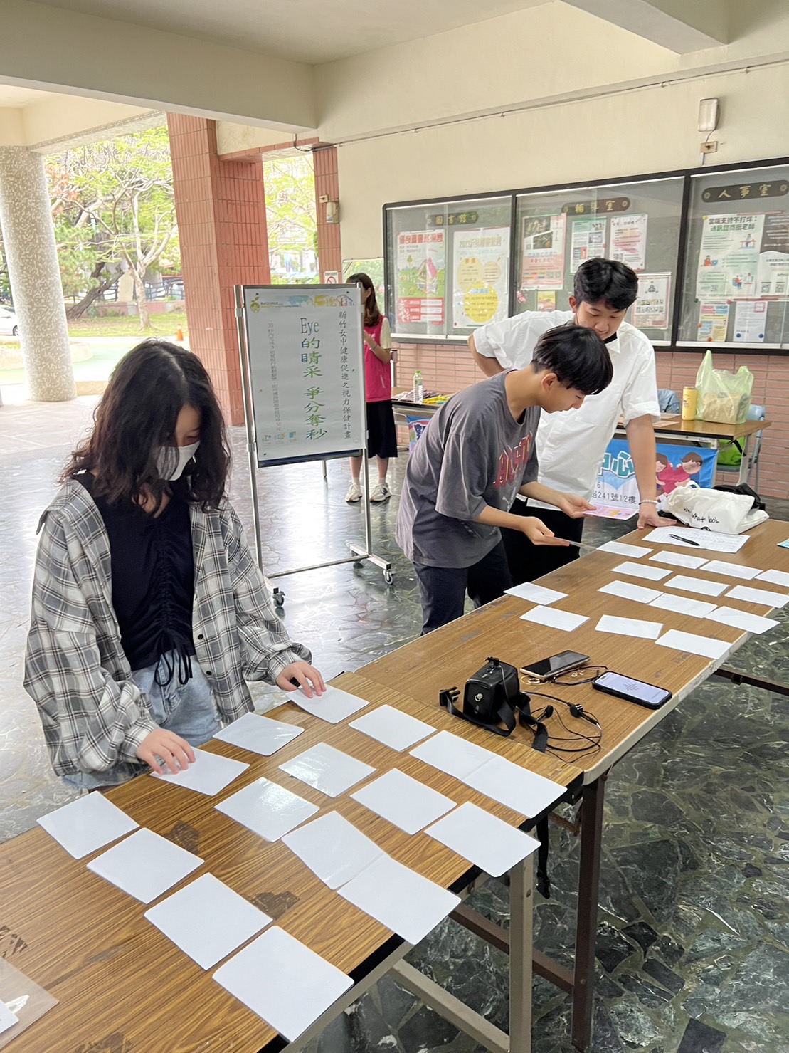 學生站在桌前翻閱健康宣導卡片，參與「EYE的睛采--爭分奪秒」卡牌配對活動。