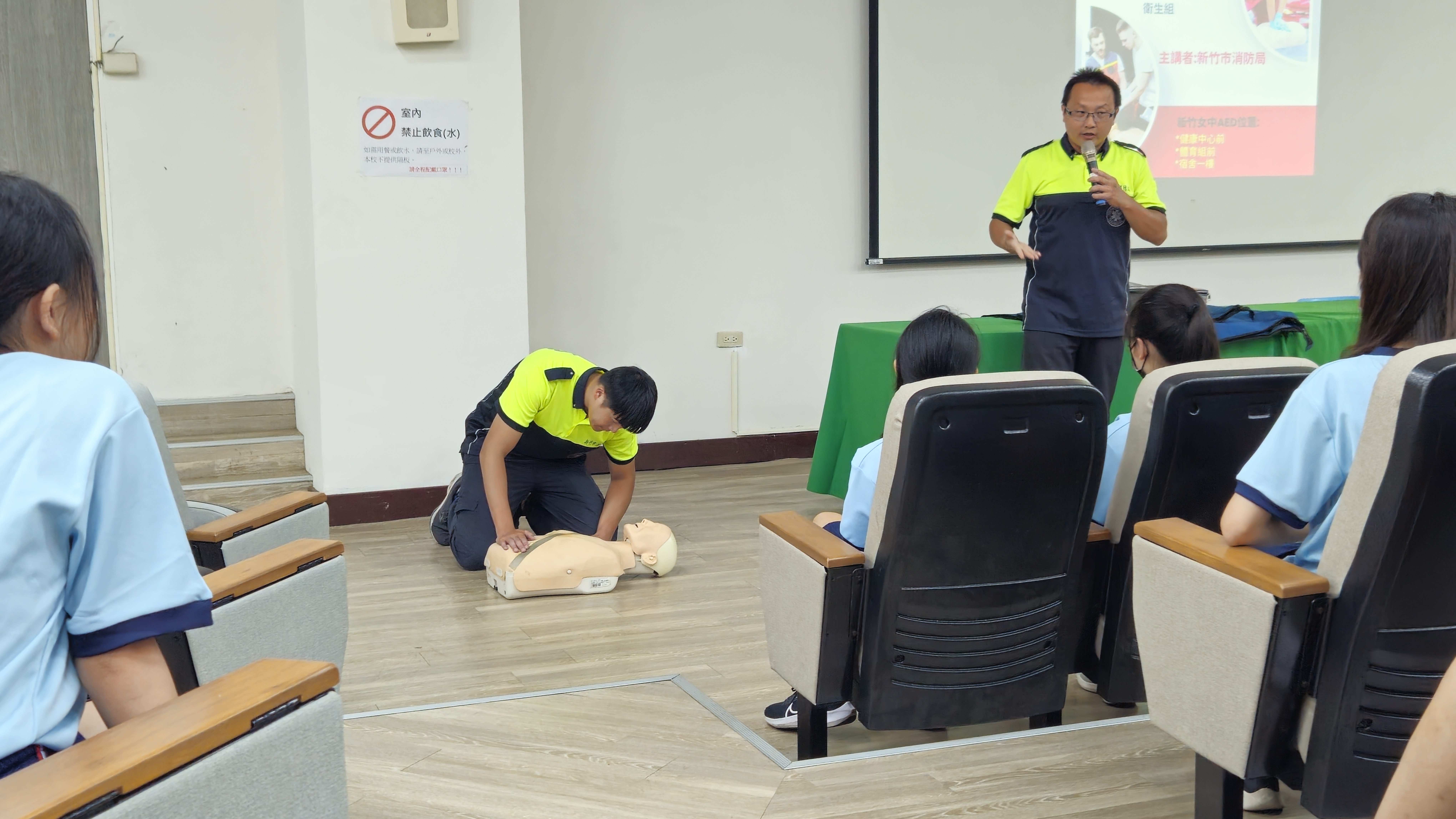 講師於前方講台示範心肺復甦術（CPR）操作步驟，學生在座位上觀看學習。