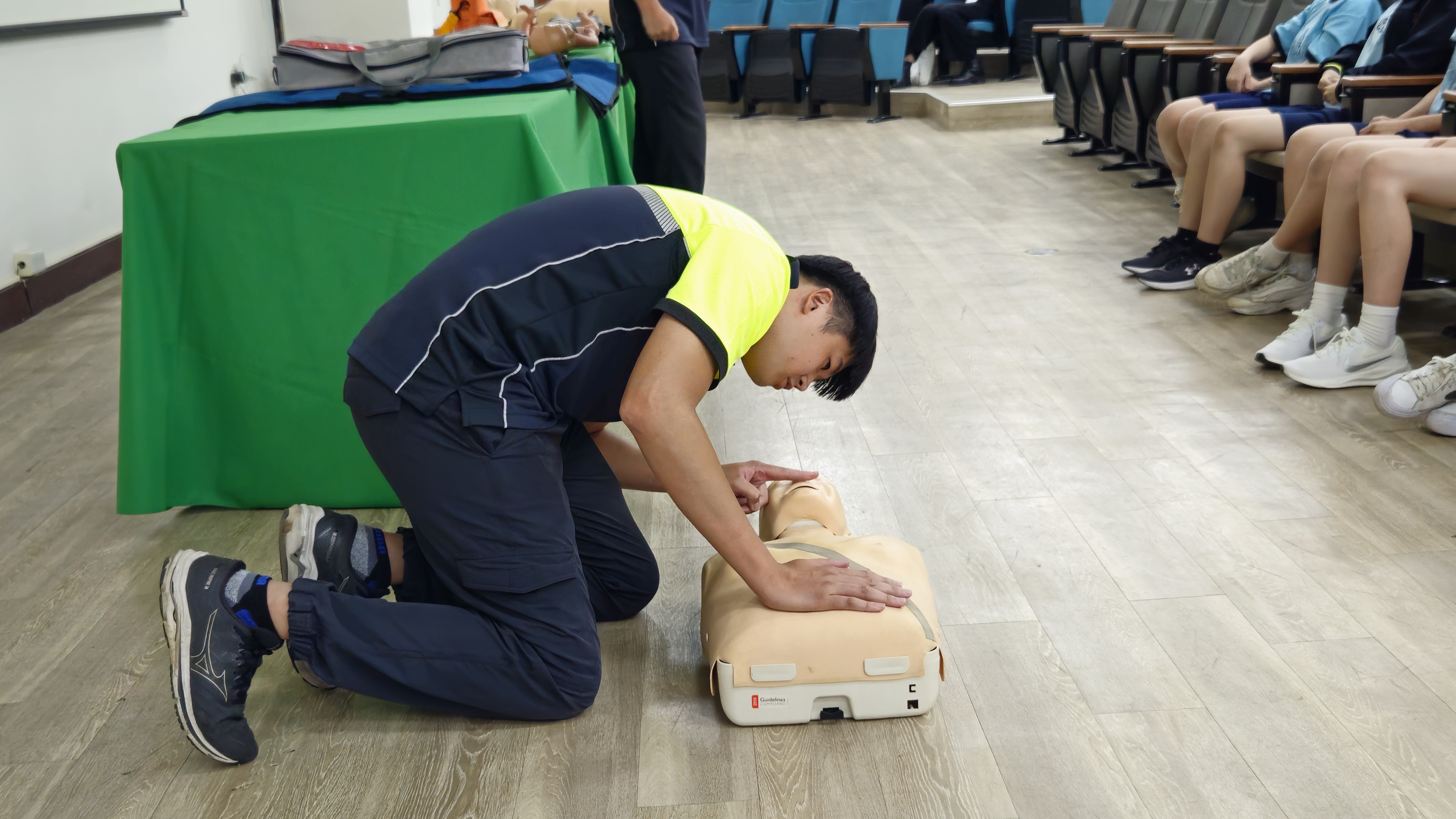 講師示範心肺復甦術（CPR）胸外按壓操作，學生圍觀學習急救技巧。