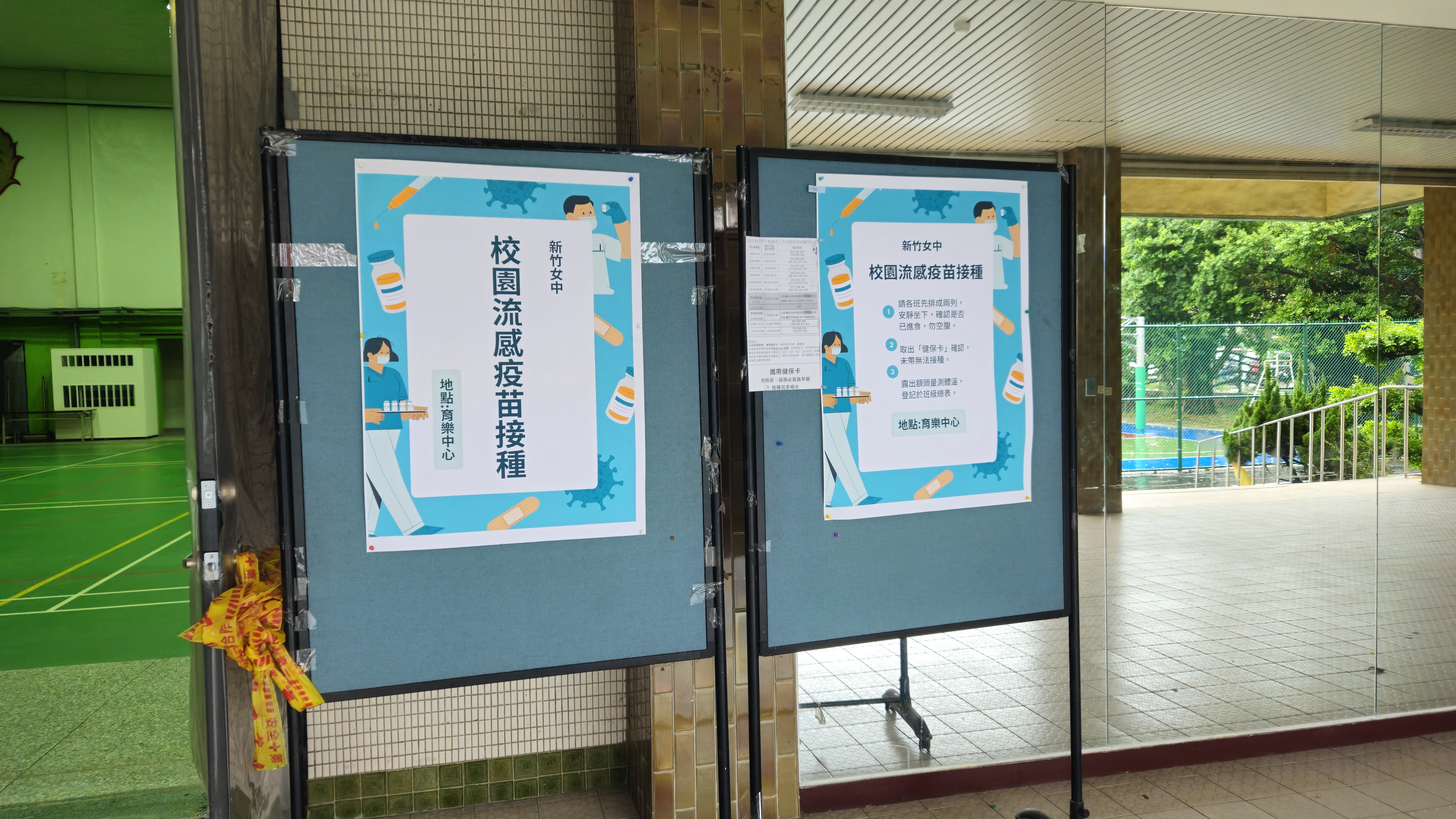 育樂中心入口處擺放著兩面藍色告示牌，上面張貼著校園流感疫苗接種的宣導海報，做為流感疫苗接種入口。